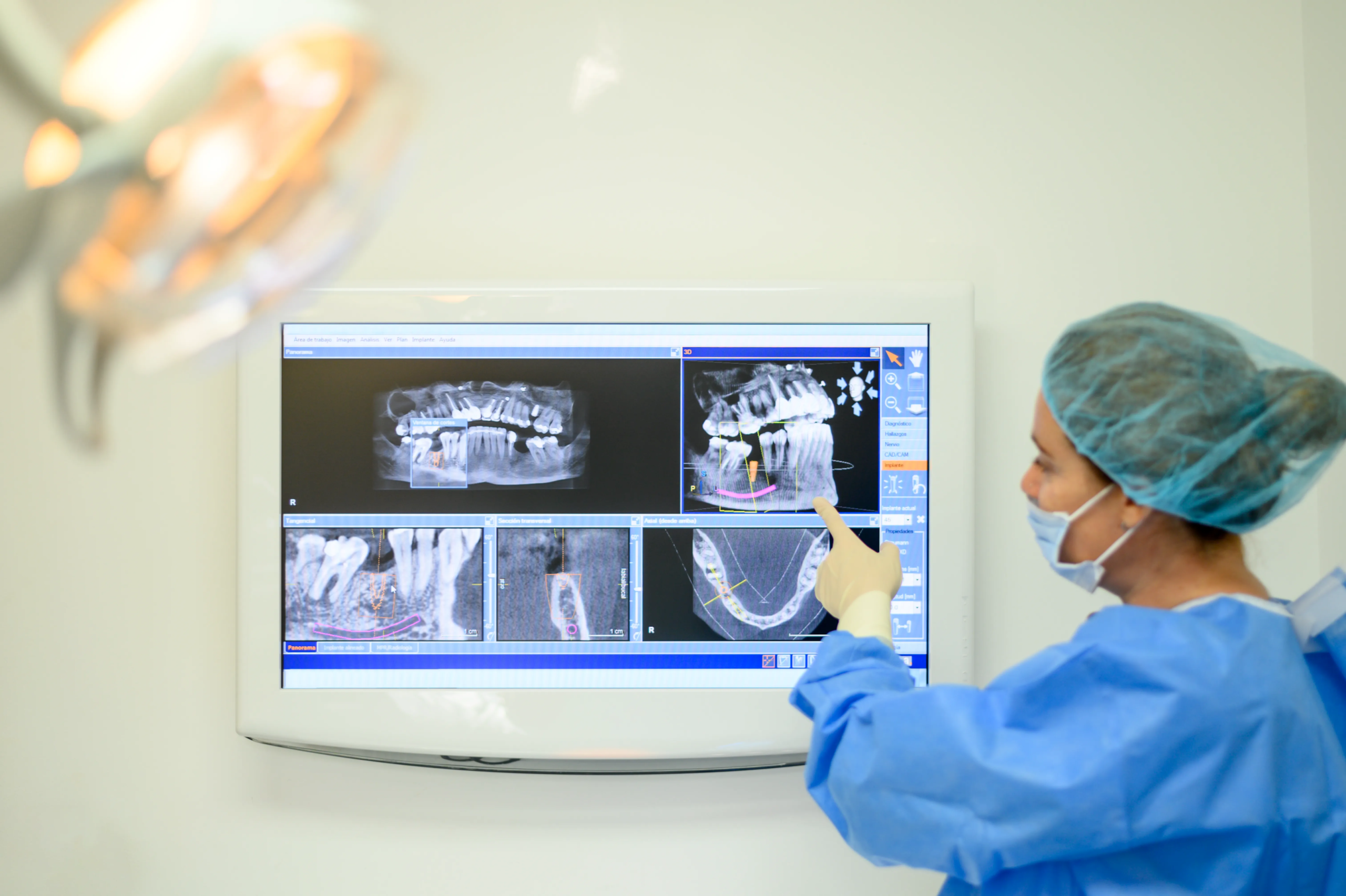 A dental professional in surgical attire examining detailed dental x-rays and scans on a monitor for implant planning.