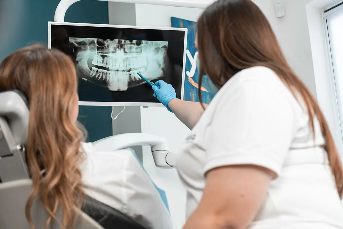 Dental professional pointing at a panoramic x-ray while explaining treatment options to a patient in a modern dental office.