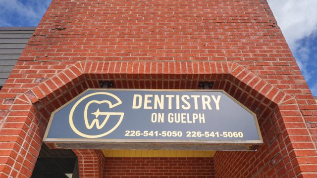 Dentistry on Guelph sign with phone numbers on brick building.